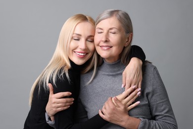 Family portrait of young woman and her mother on grey background