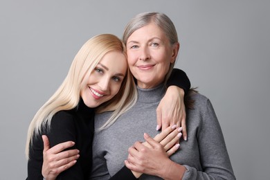 Family portrait of young woman and her mother on grey background