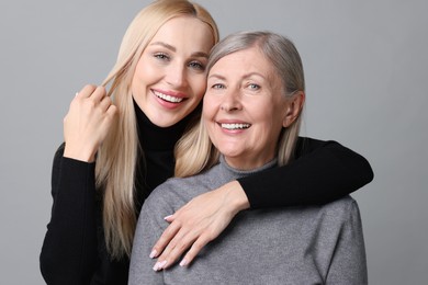 Family portrait of young woman and her mother on grey background