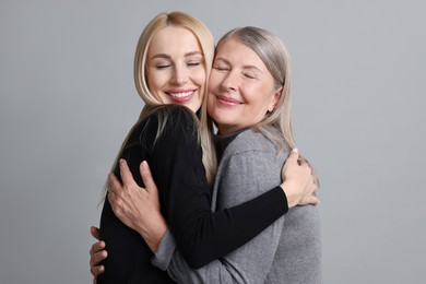 Family portrait of young woman and her mother on grey background