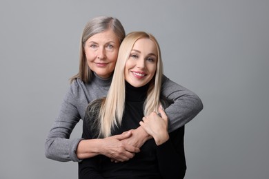 Family portrait of young woman and her mother on grey background