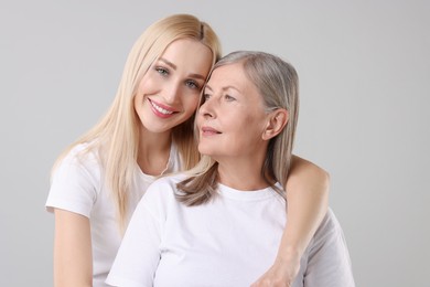 Family portrait of young woman and her mother on light grey background