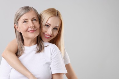 Family portrait of young woman and her mother on light grey background. Space for text