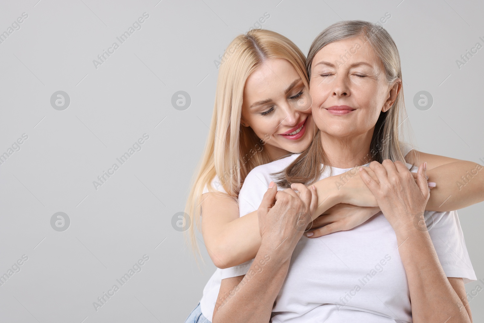 Photo of Family portrait of young woman and her mother on light grey background. Space for text