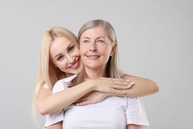 Family portrait of young woman and her mother on light grey background