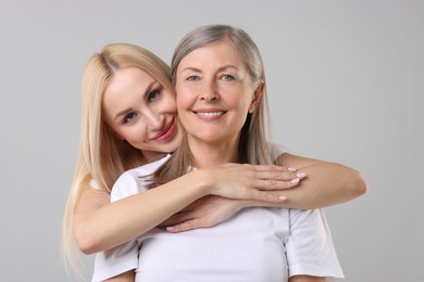 Family portrait of young woman and her mother on light grey background