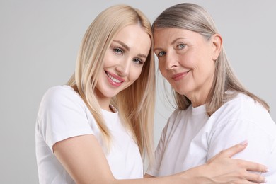 Family portrait of young woman and her mother on light grey background