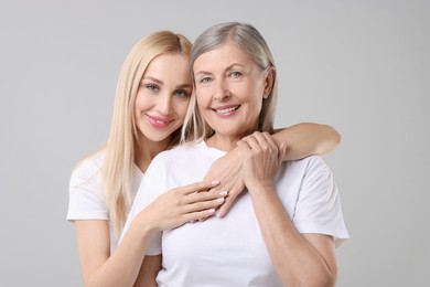 Family portrait of young woman and her mother on light grey background