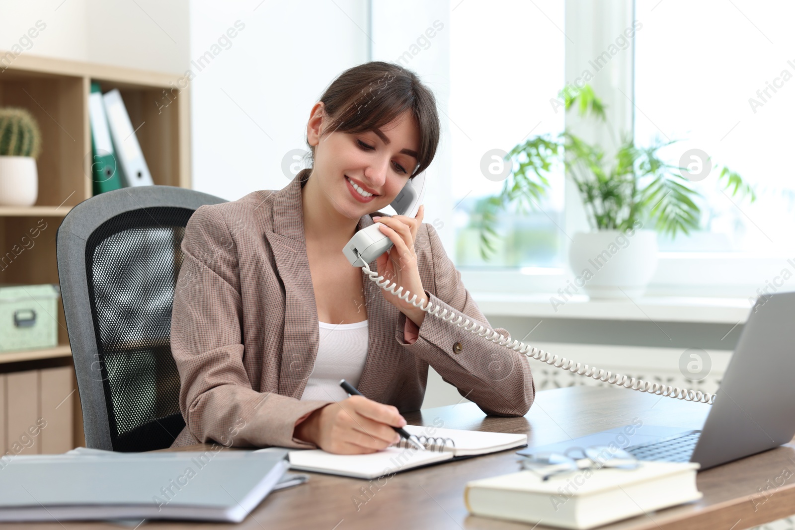 Photo of Smiling secretary talking on telephone at table in office