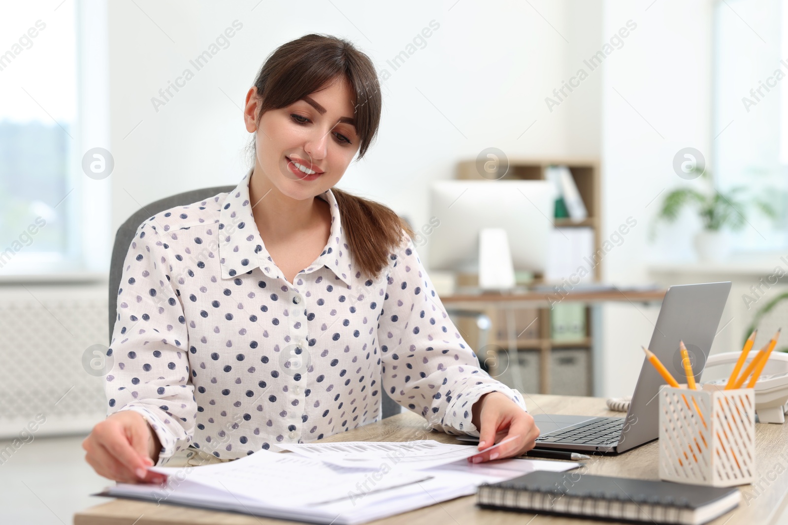 Photo of Smiling secretary doing paperwork at table in office