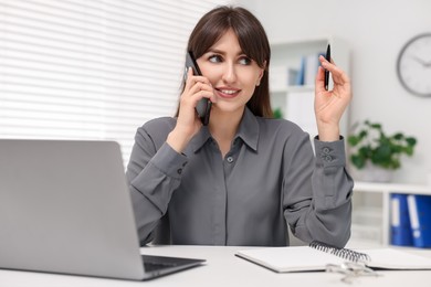 Smiling secretary talking by smartphone at table in office