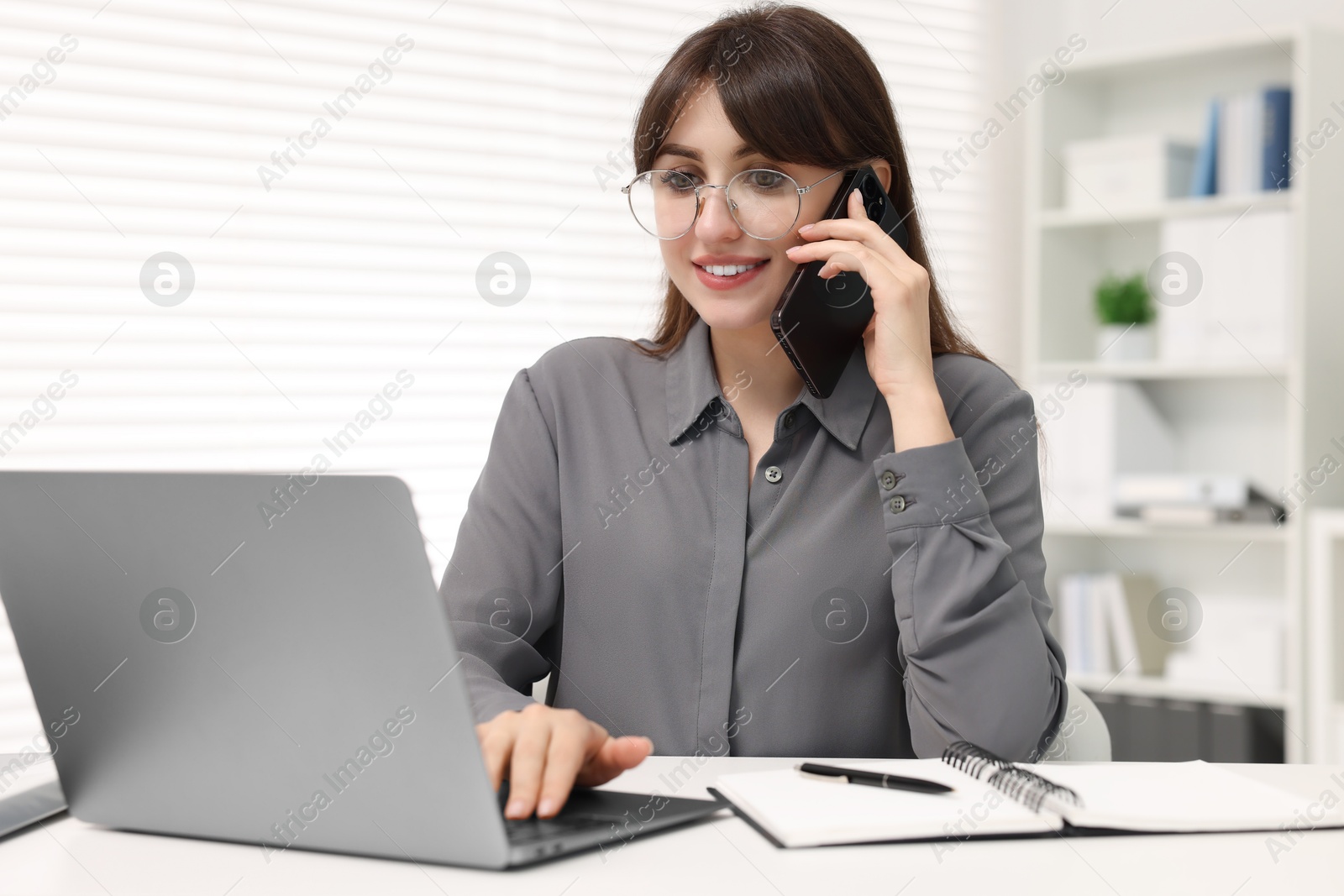 Photo of Smiling secretary talking by smartphone at table in office