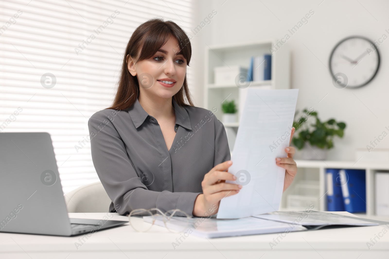 Photo of Smiling secretary doing paperwork at table in office