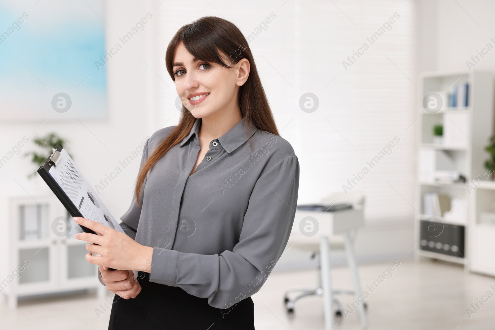 Photo of Portrait of smiling secretary with clipboard in office. Space for text