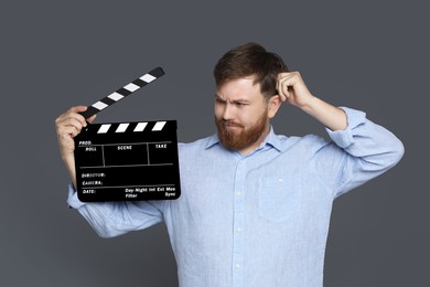 Making movie. Thoughtful man with clapperboard on grey background