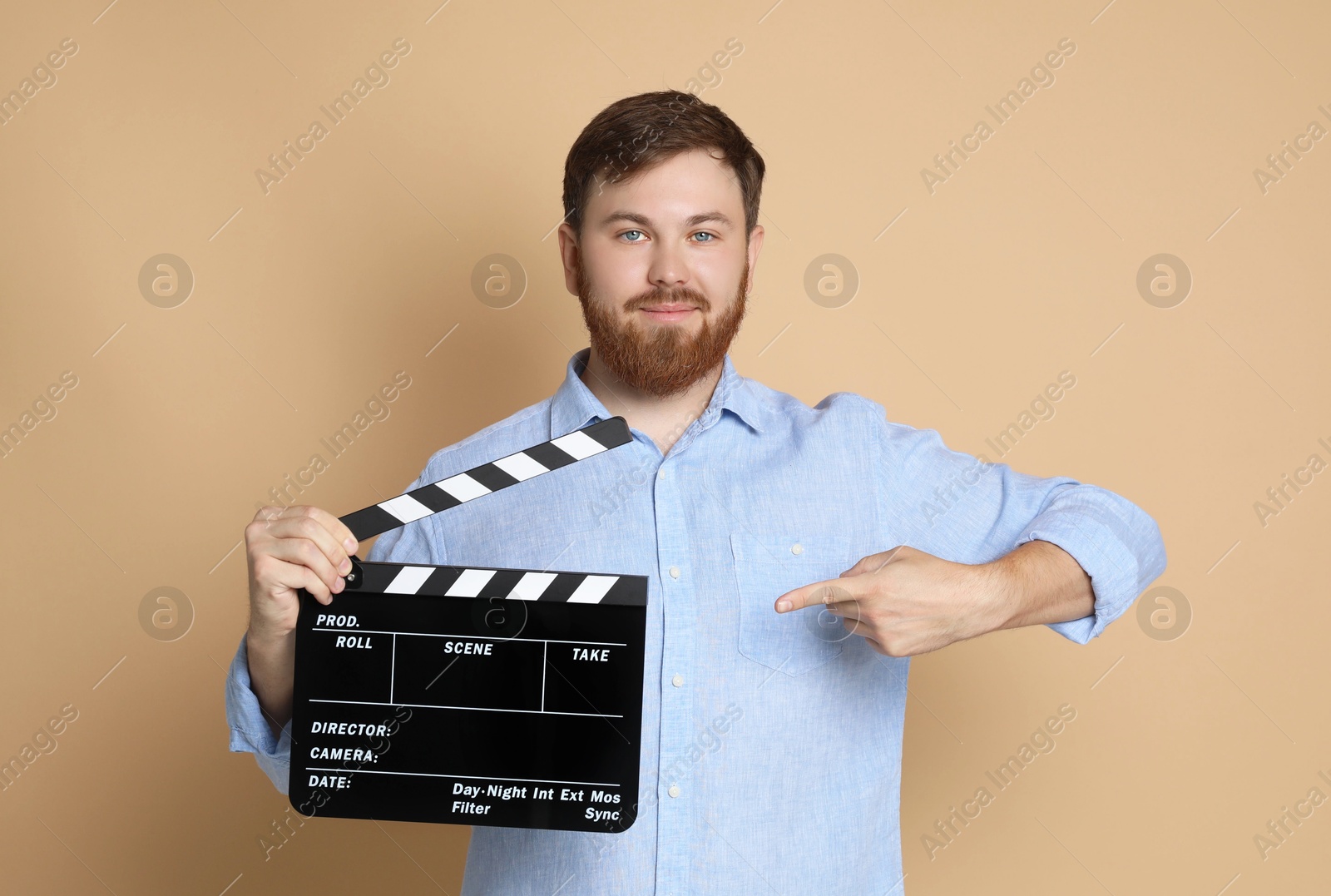 Photo of Making movie. Man pointing at clapperboard on beige background