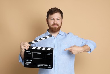 Making movie. Man pointing at clapperboard on beige background