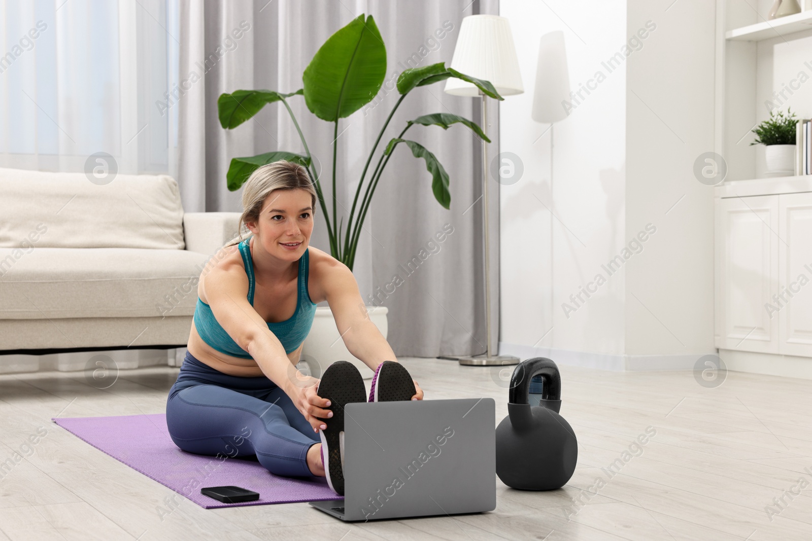 Photo of Online fitness trainer. Woman doing exercise near laptop at home