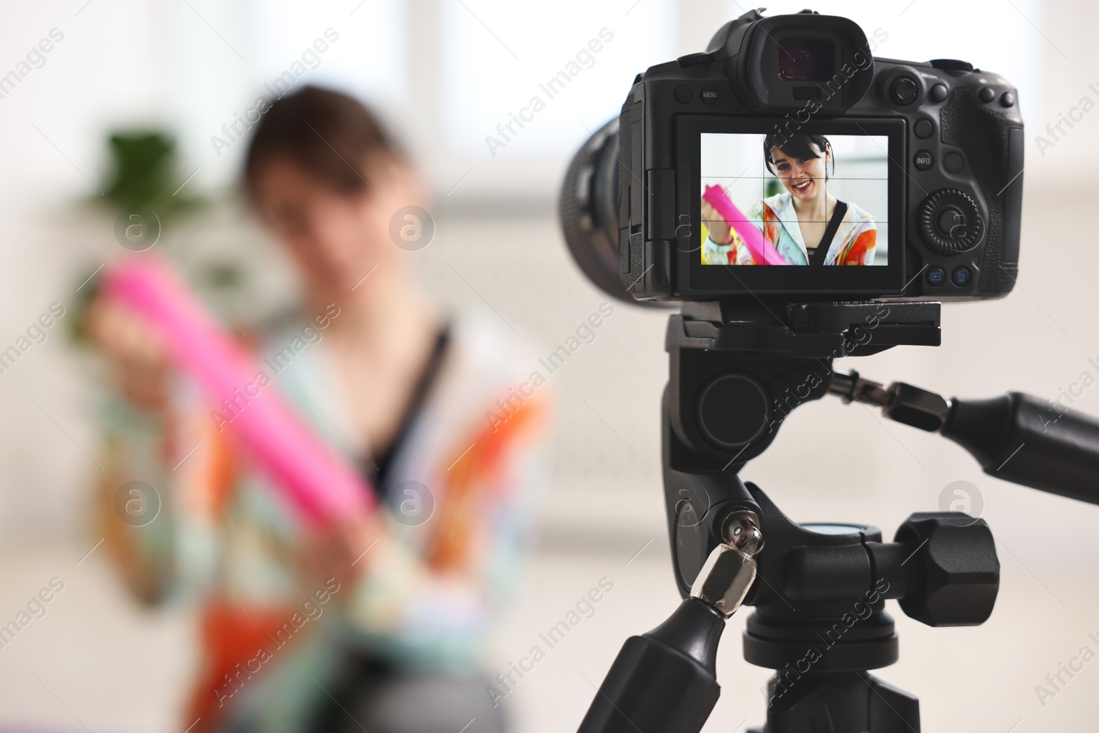 Photo of Happy sports blogger with resistance band recording fitness lesson at home, focus on camera