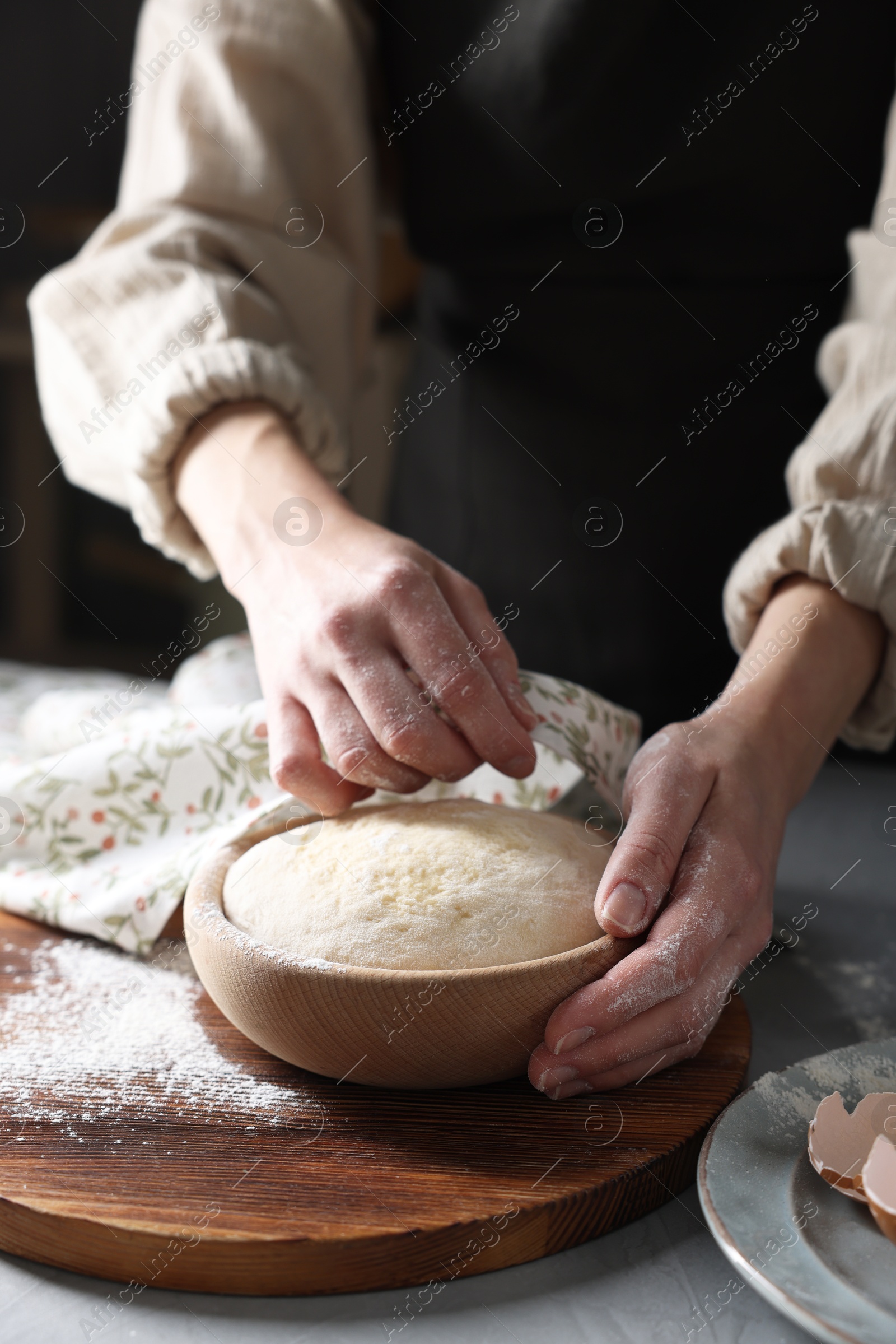 Photo of Woman covering dough with napkin at grey table, closeup