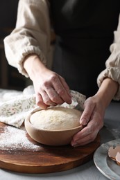 Woman covering dough with napkin at grey table, closeup