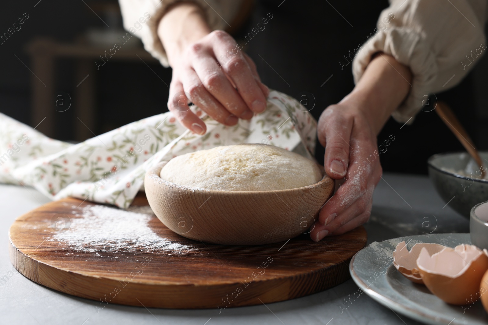 Photo of Woman covering dough with napkin at grey table, closeup