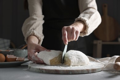 Woman cutting dough at grey table, closeup