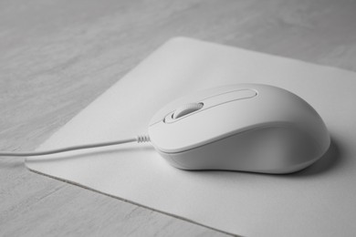 Wired mouse with mousepad on grey wooden table, closeup