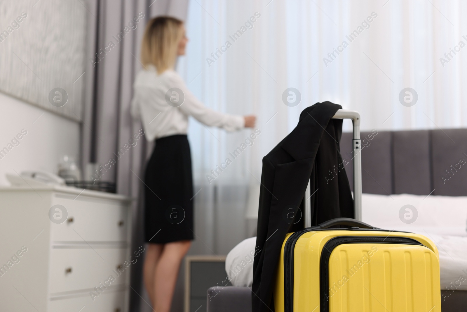 Photo of Guest opening curtains in stylish hotel room, focus on suitcase