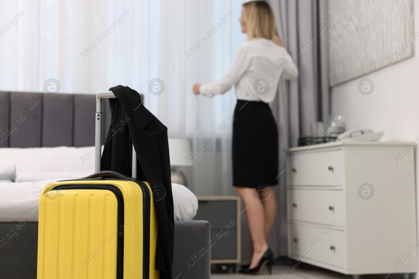 Photo of Guest opening curtains in stylish hotel room, focus on suitcase