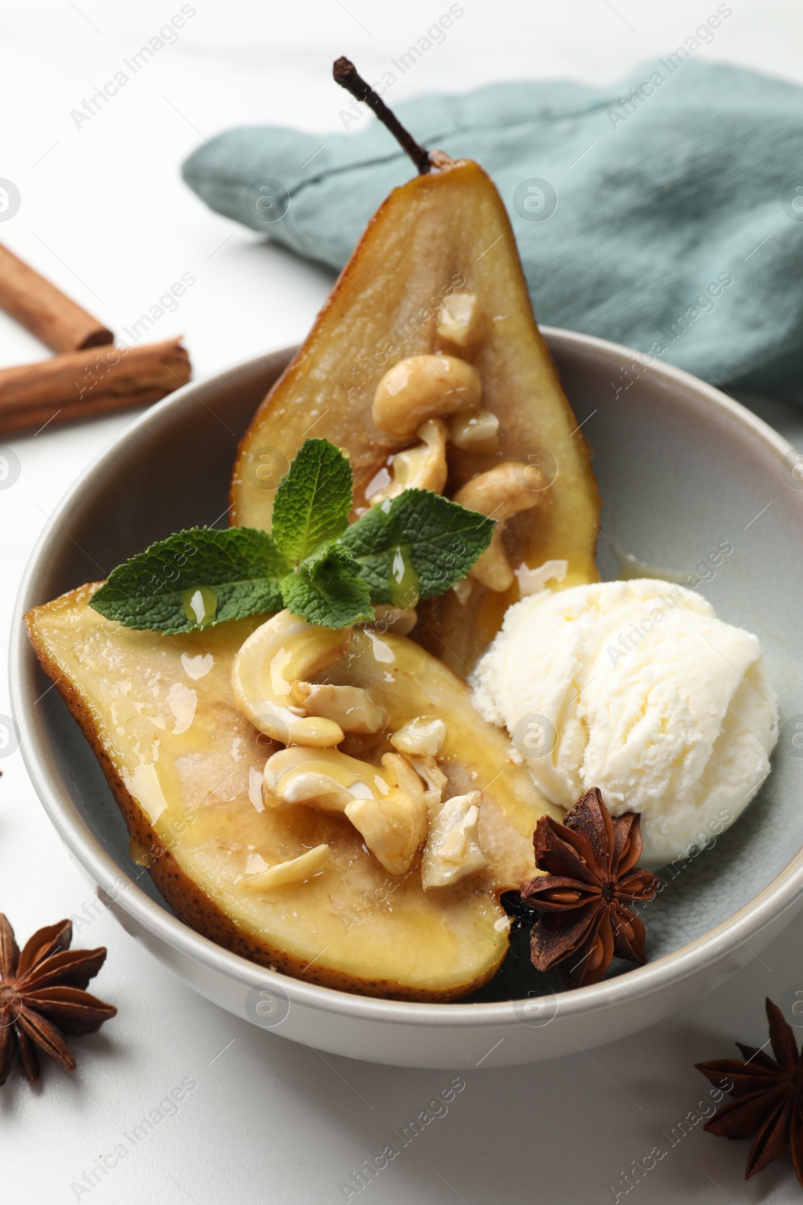 Photo of Delicious baked pears with nuts, ice cream, anise stars, mint and honey in bowl on white table, closeup