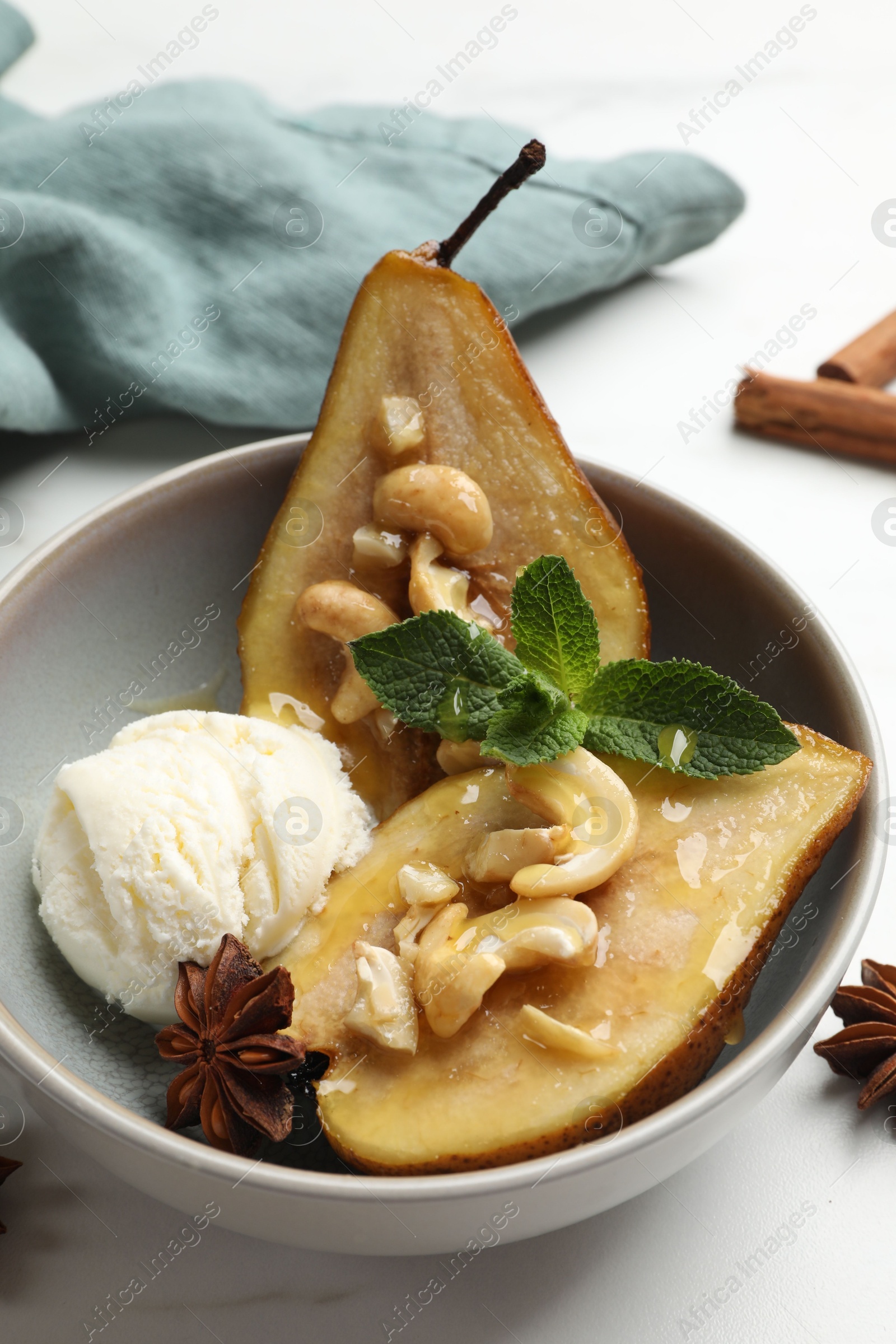 Photo of Delicious baked pears with nuts, ice cream, anise stars, mint and honey in bowl on white table, closeup