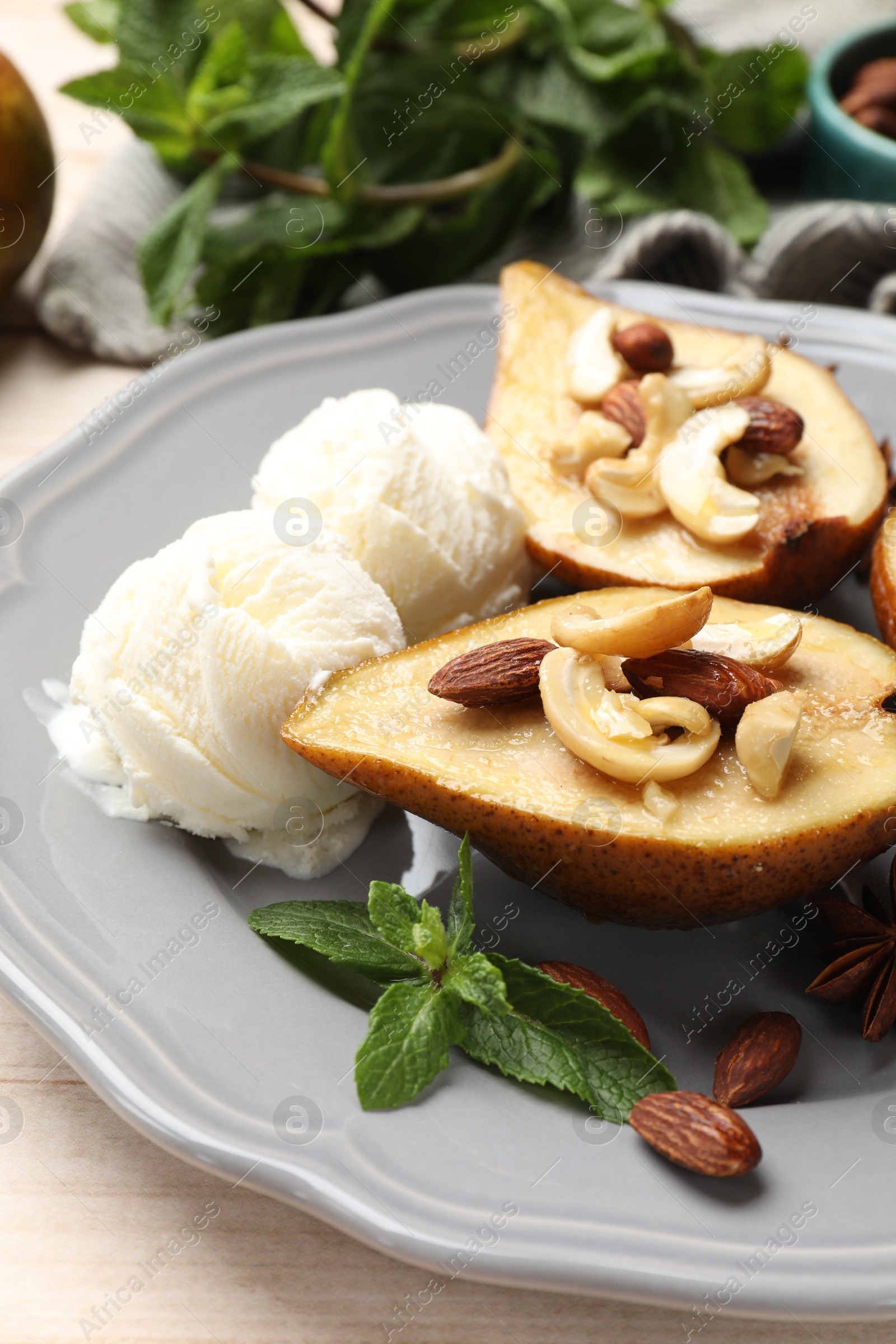 Photo of Delicious baked pears with nuts, ice cream, mint and honey on light wooden table, closeup