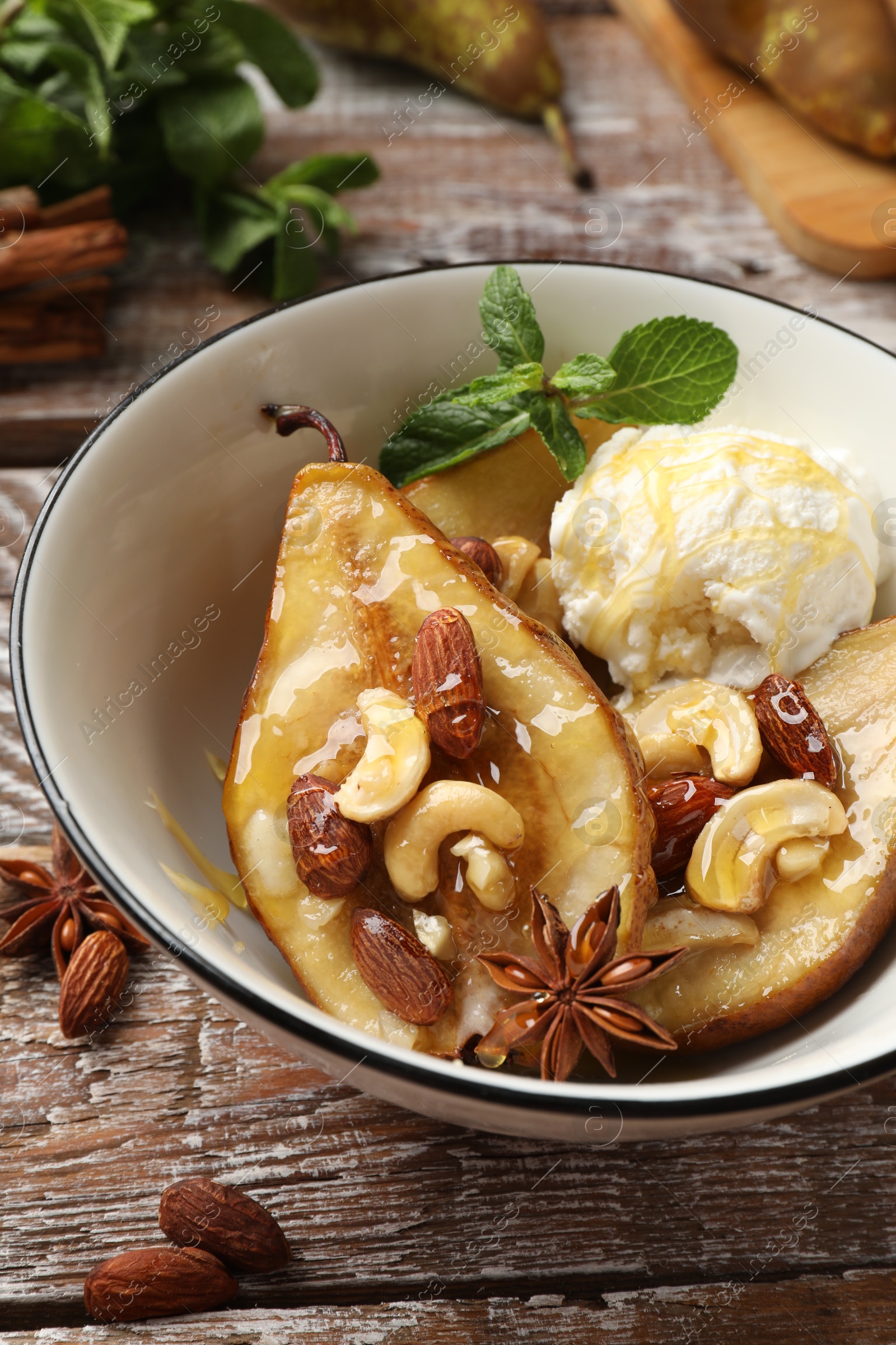 Photo of Delicious baked pears with nuts, ice cream, anise stars and honey in bowl on wooden rustic table, closeup