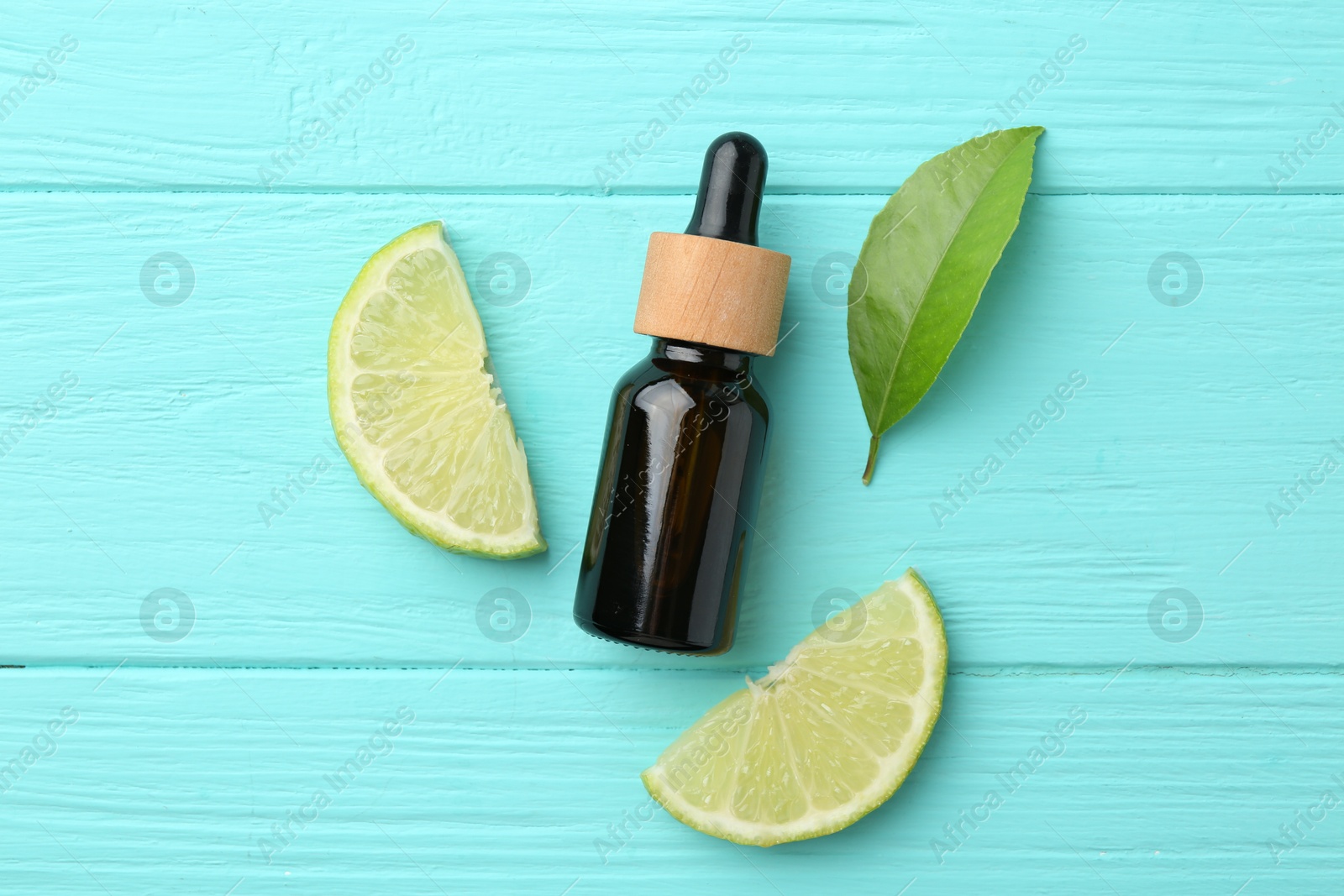 Photo of Bottle of essential oil, lime and green leaf on turquoise wooden table, flat lay