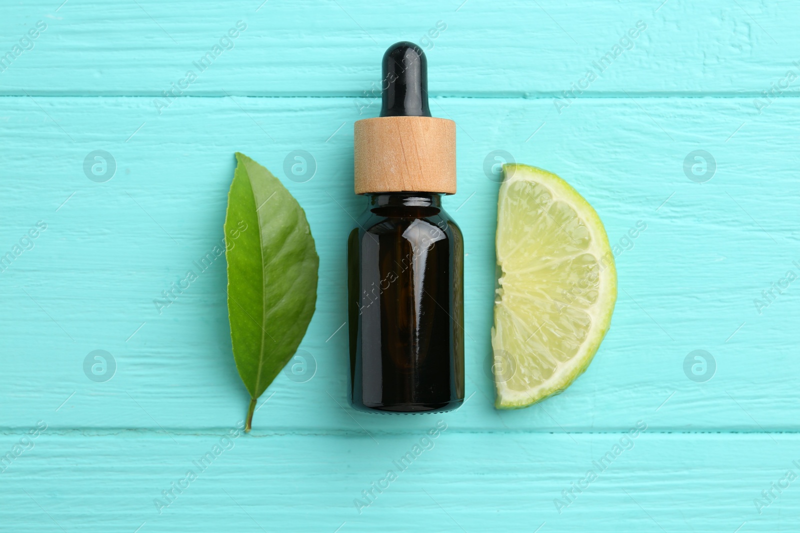 Photo of Bottle of essential oil, lime and green leaf on turquoise wooden table, flat lay