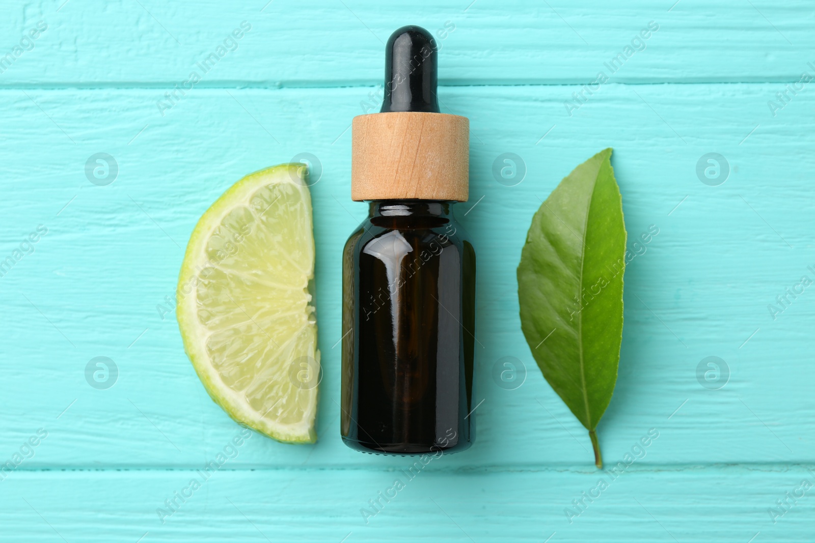 Photo of Bottle of essential oil, lime and green leaf on turquoise wooden table, flat lay