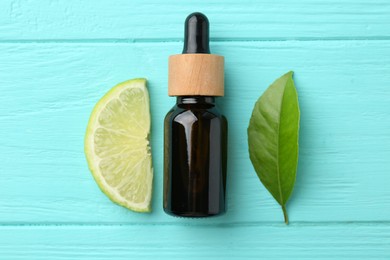 Photo of Bottle of essential oil, lime and green leaf on turquoise wooden table, flat lay