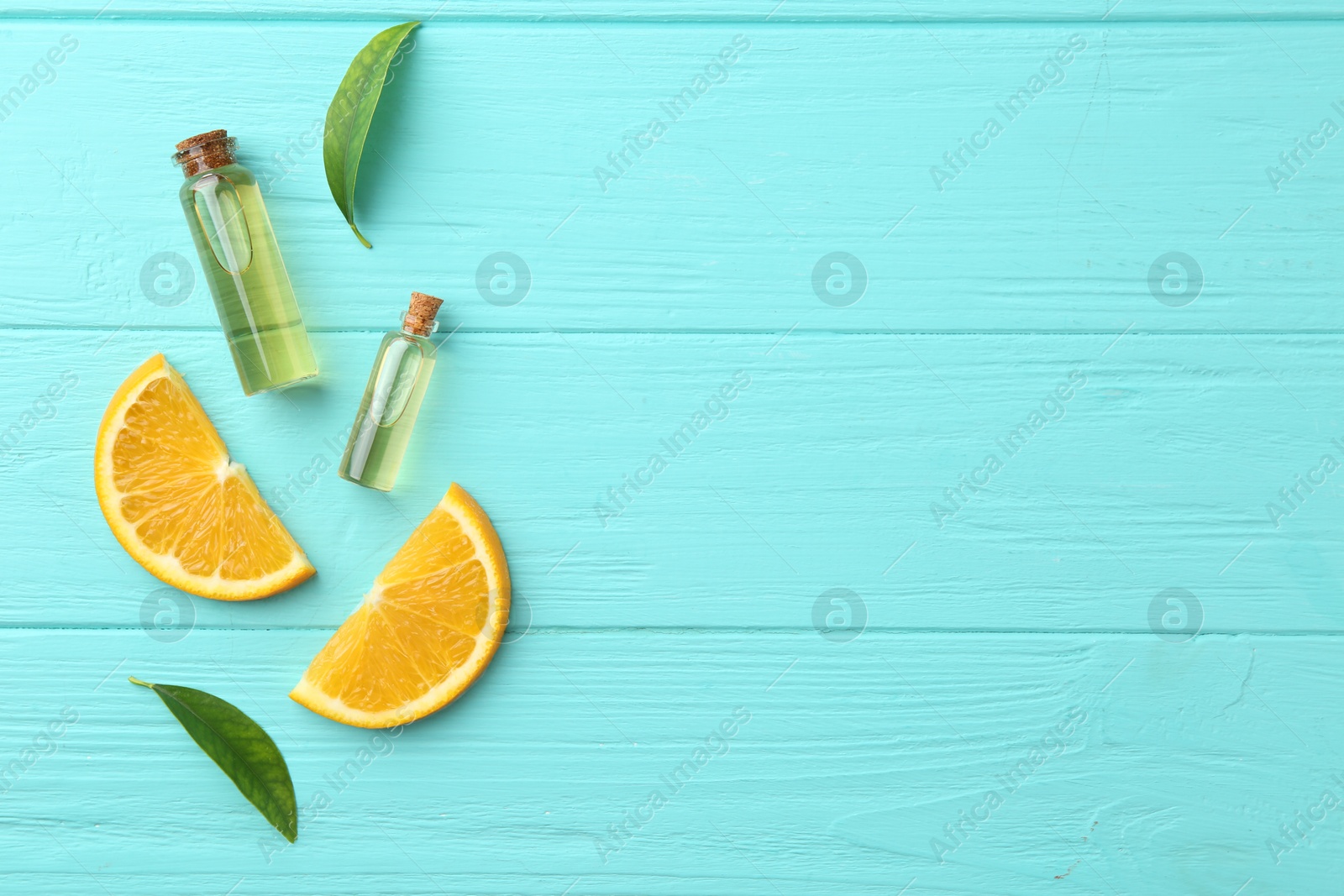 Photo of Bottles of essential oils, orange and green leaves on turquoise wooden table, flat lay. Space for text