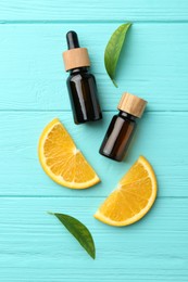 Bottles of essential oils, orange and green leaves on turquoise wooden table, flat lay