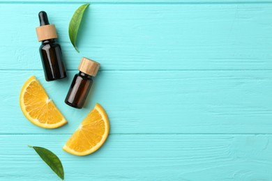 Photo of Bottles of essential oils, orange and green leaves on turquoise wooden table, flat lay. Space for text