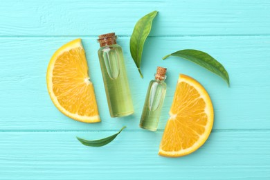 Bottles of essential oils, orange and green leaves on turquoise wooden table, flat lay