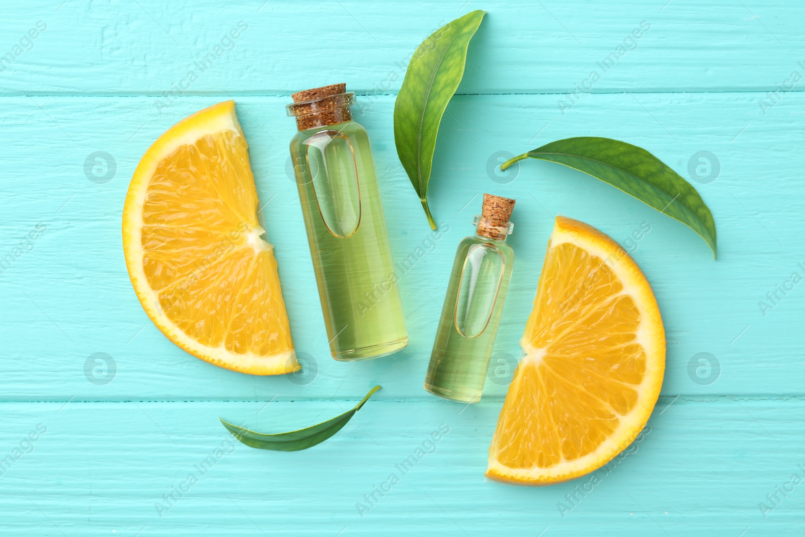 Photo of Bottles of essential oils, orange and green leaves on turquoise wooden table, flat lay