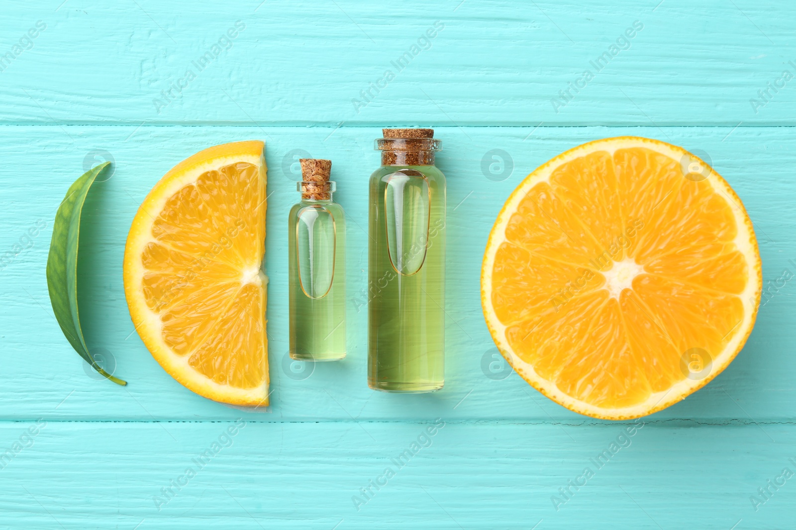 Photo of Bottles of essential oils, orange and green leaf on turquoise wooden table, flat lay