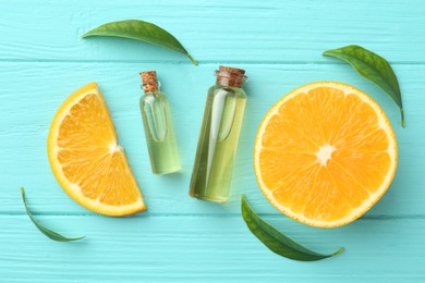 Bottles of essential oils, orange and green leaves on turquoise wooden table, flat lay