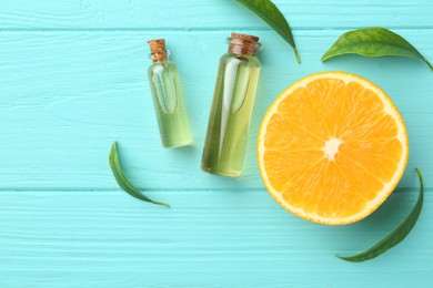 Photo of Bottles of essential oils, orange and green leaves on turquoise wooden table, flat lay