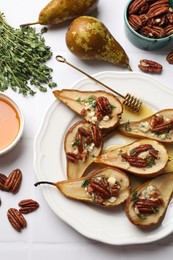 Delicious baked pears with nuts, blue cheese, thyme and honey on white tiled table, flat lay