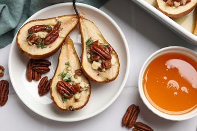 Delicious baked pears with nuts, blue cheese, thyme and honey on white tiled table, flat lay