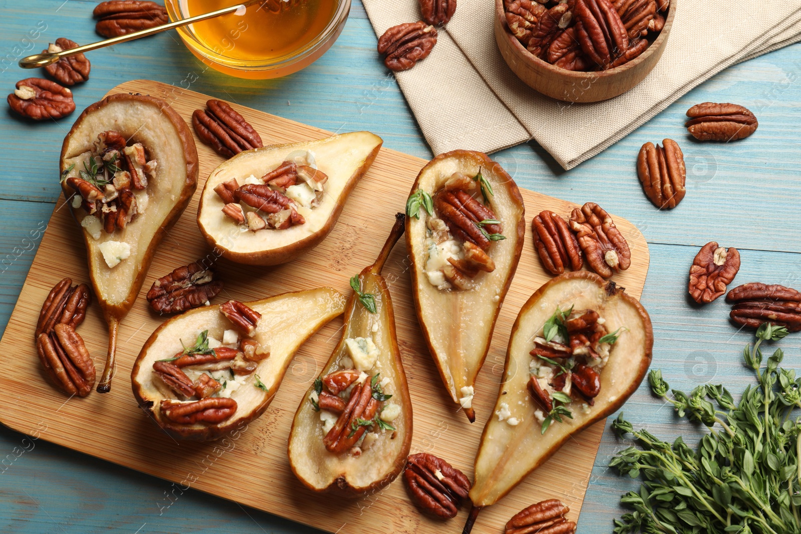 Photo of Delicious baked pears with nuts, blue cheese, thyme and honey on light blue wooden table, flat lay