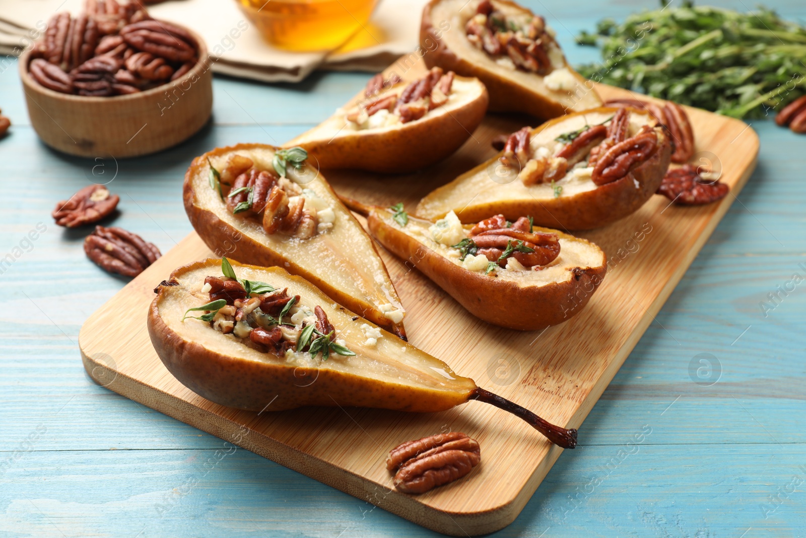 Photo of Delicious baked pears with nuts, blue cheese, thyme and honey on light blue wooden table, closeup